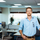 Young handsome successful businessman smiling, posing, office background